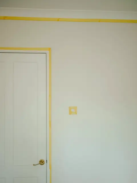Mur blanc et porte, bande d’adhésif jaune posée le long des angles avant la peinture