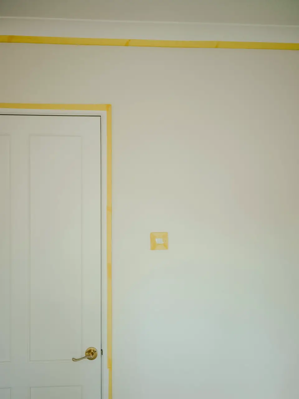 Mur blanc et porte, bande d’adhésif jaune posée le long des angles avant la peinture
