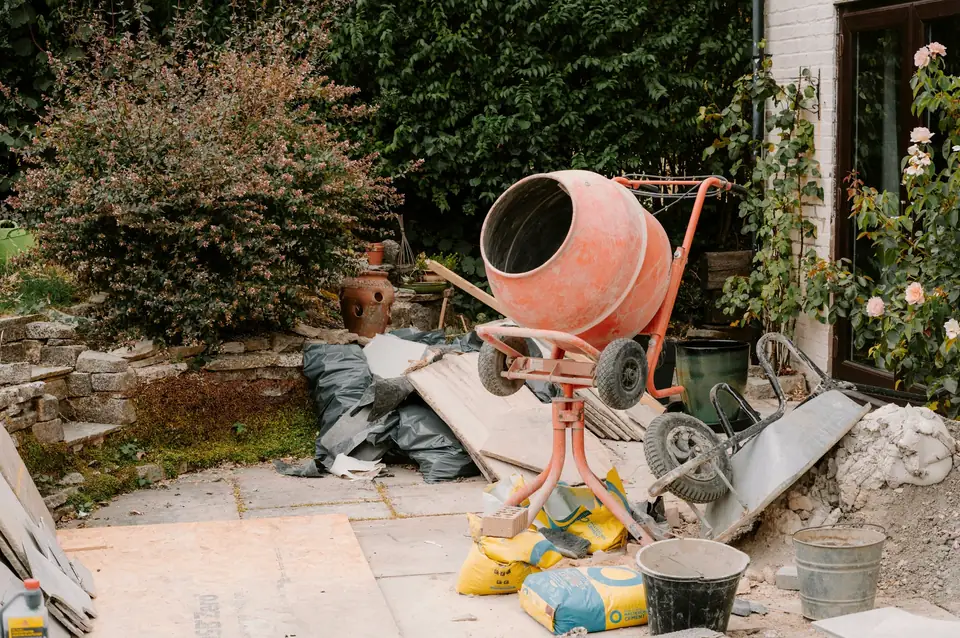 Bétonnière orange, brouette et sacs de ciment sur une terrasse de jardin en travaux