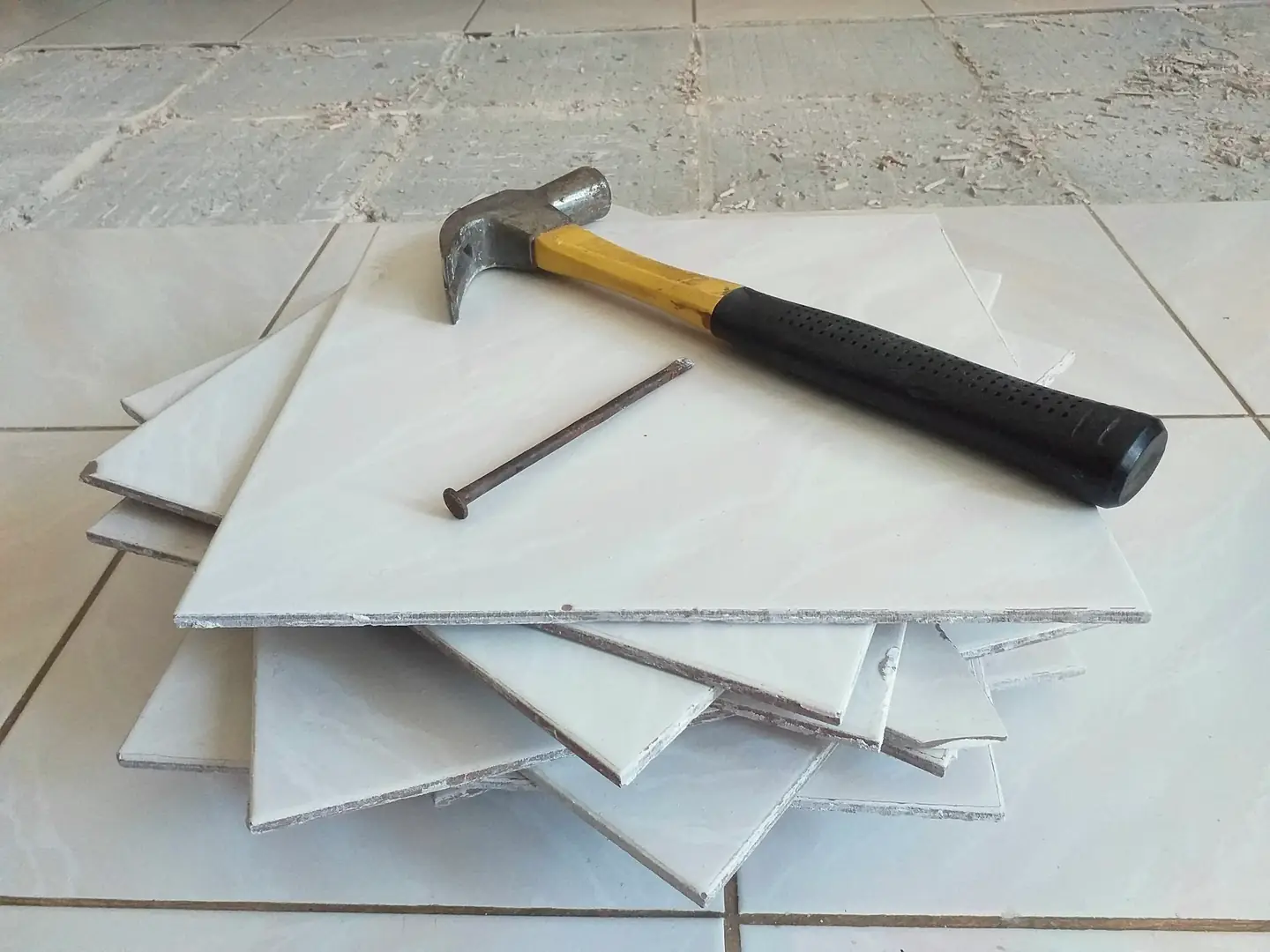 Pile de carreaux clairs et marteau posés sur un sol en cours de pose