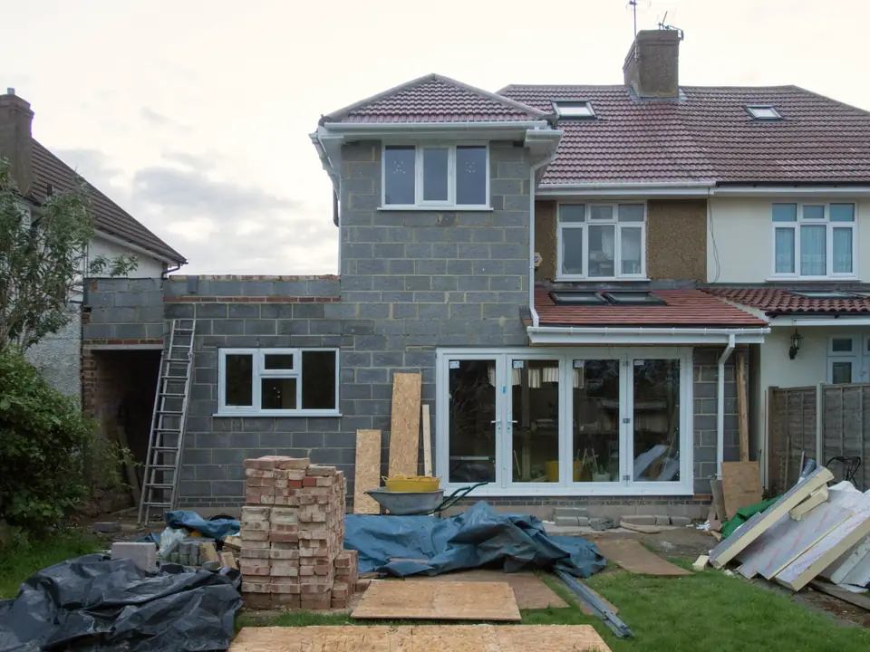 Extension en blocs béton accolée à une maison, matériaux et briques stockés dans le jardin