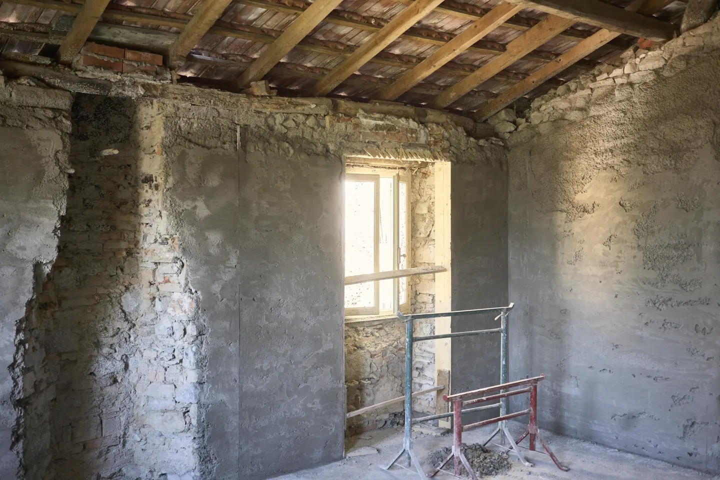 Intérieur d’une maison ancienne mis à nu : murs de pierre, solives apparentes et fenêtre ouverte