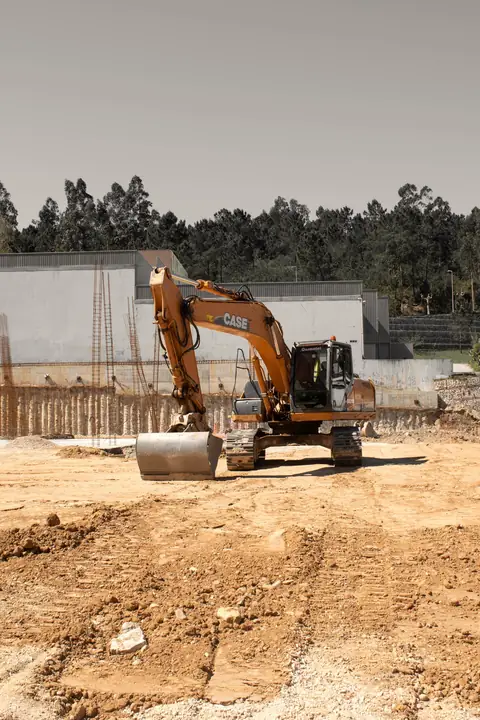 Pelle mécanique orange sur un terrain de chantier décapé, tas de terre au premier plan