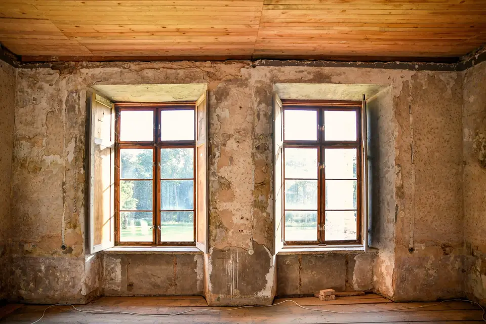 Pièce ancienne vide, murs de pierre enduits à la chaux, deux fenêtres à petits bois et plafond en planches