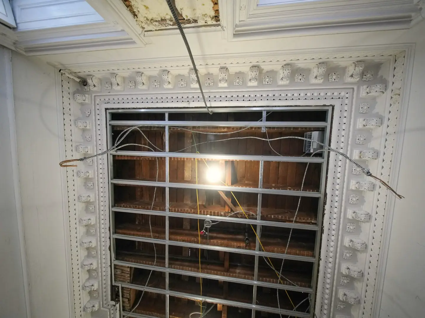 Plafond orné de moulures blanches en cours de restauration, ossature métallique visible au centre
