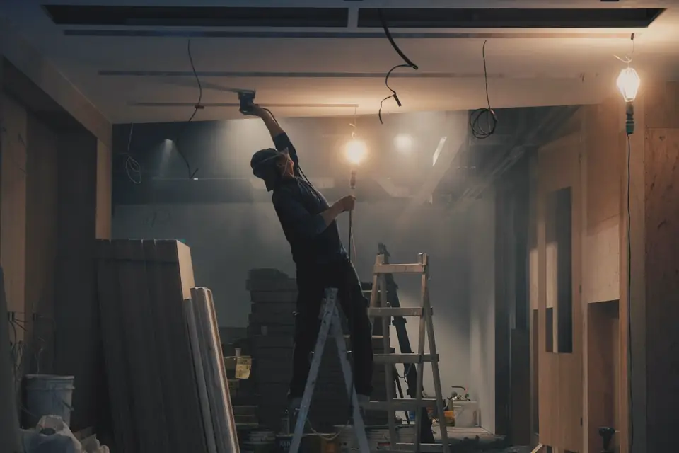 Ouvrier monté sur un escabeau qui travaille au plafond d’une pièce en chantier