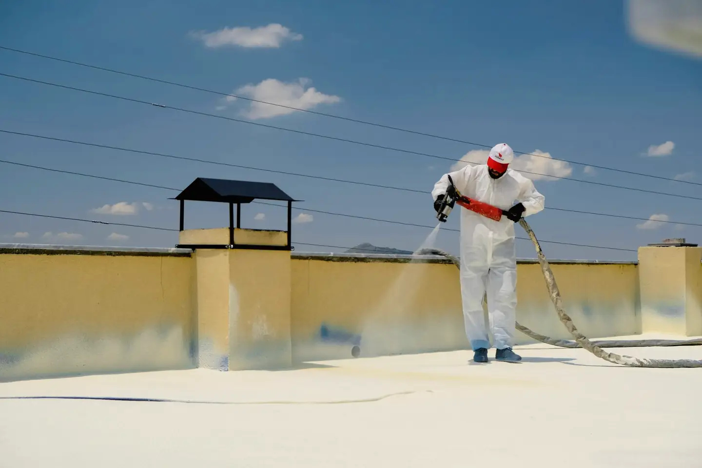 Opérateur en combinaison blanche qui pulvérise un produit sur une toiture-terrasse
