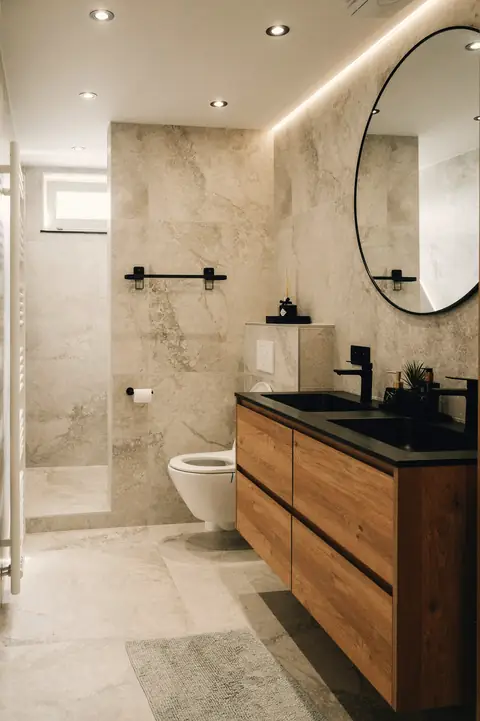 Salle de bain carrelée en grand format clair, meuble vasque en bois et miroir rond