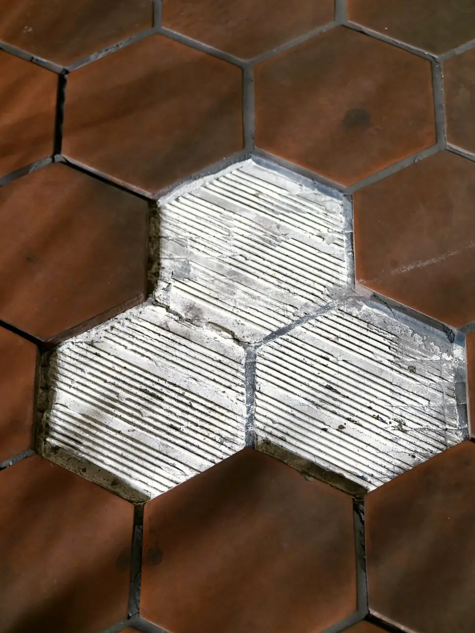 Sol de tomettes hexagonales en terre cuite : trois carreaux manquants laissent voir les sillons de colle