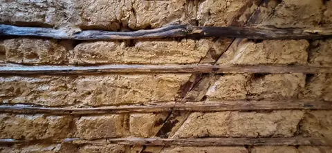 Gros plan d’un remplissage en terre et paille sur lattis de bois, entre deux pièces de charpente